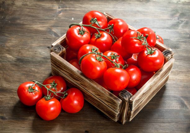 Fresh tomatoes in a box. On a wooden table.
