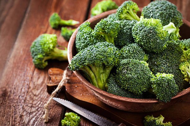 Fresh raw green broccoli in bowl on rustic wooden background